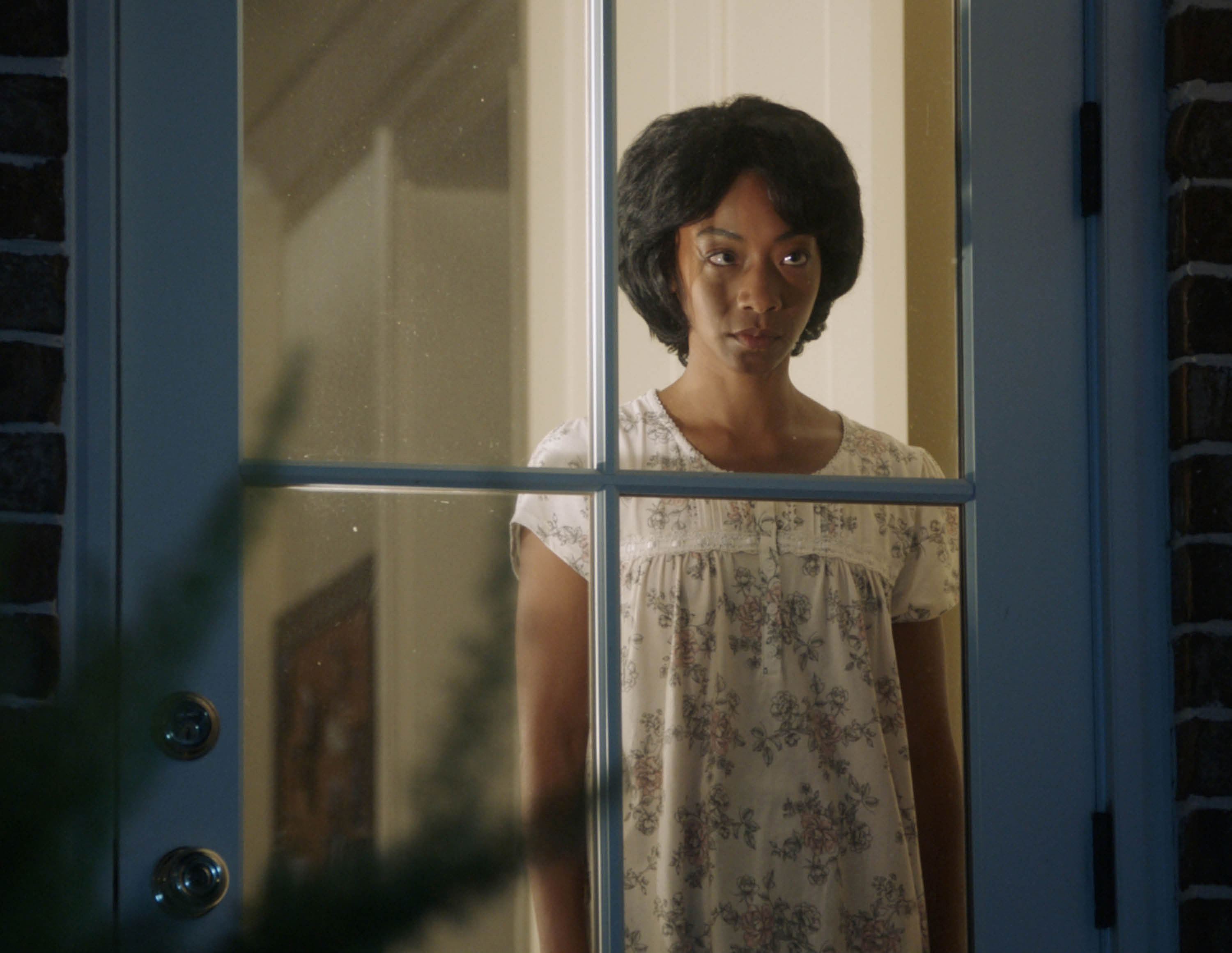 Betty Gabriel in 2017 film GET OUT standing and looking out glass-paneled door.