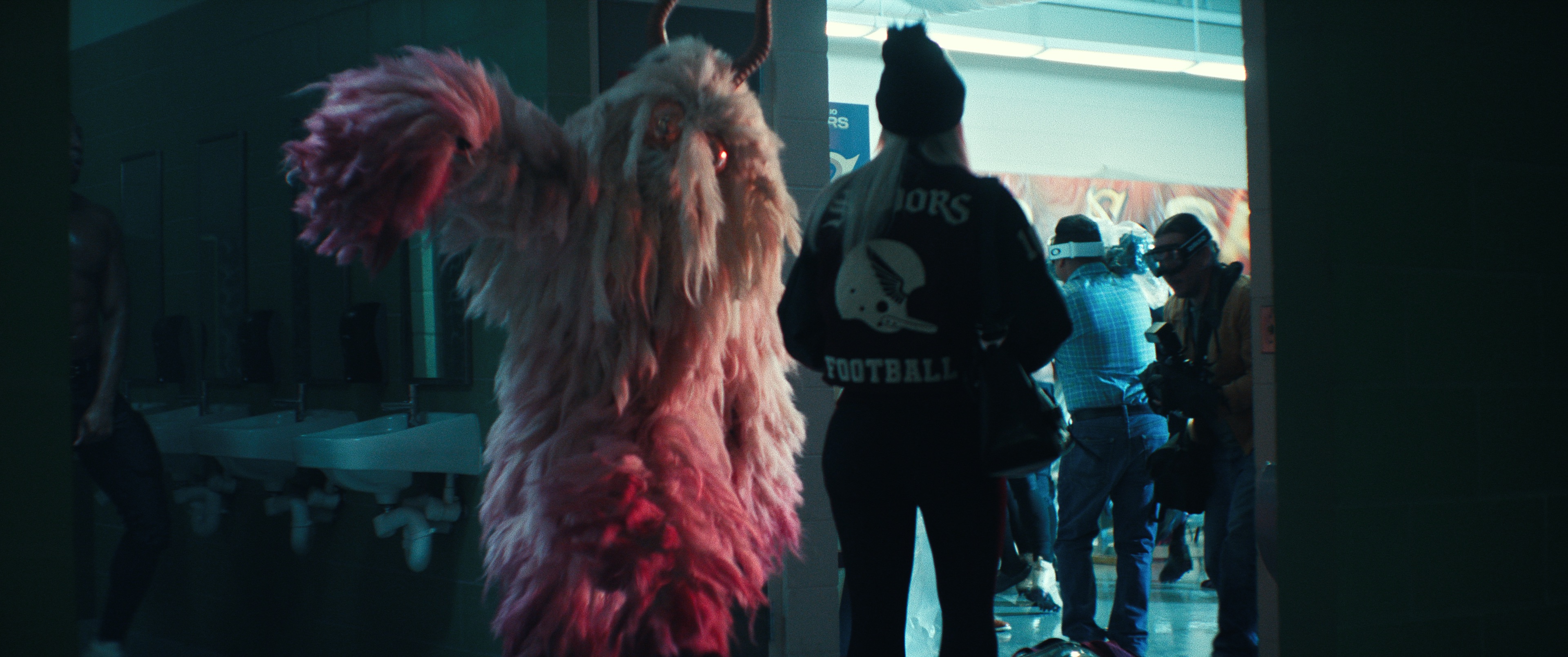 A shaggy, pink, goat-like sports mascot figure reaches towards the camera.