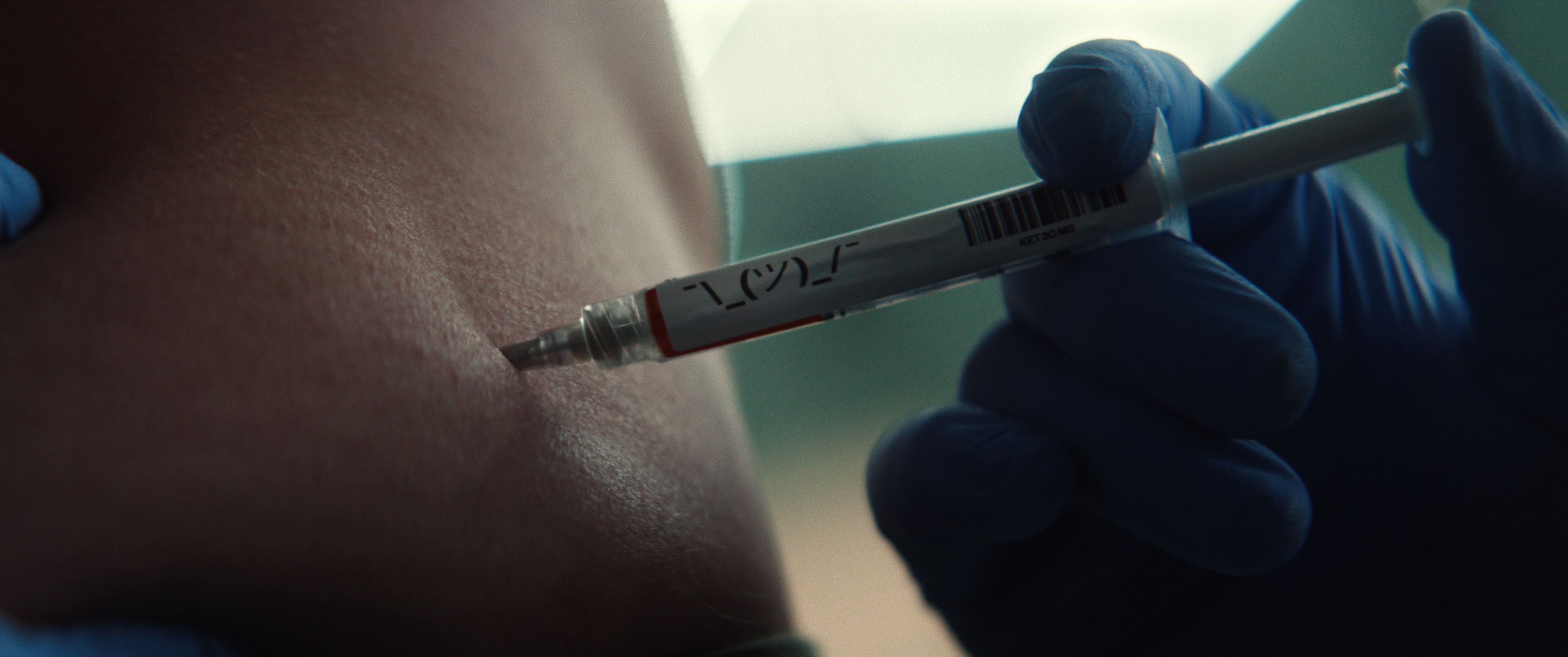 Close up of a blue medical-gloved hand inserting a hypodermic needle into skin.