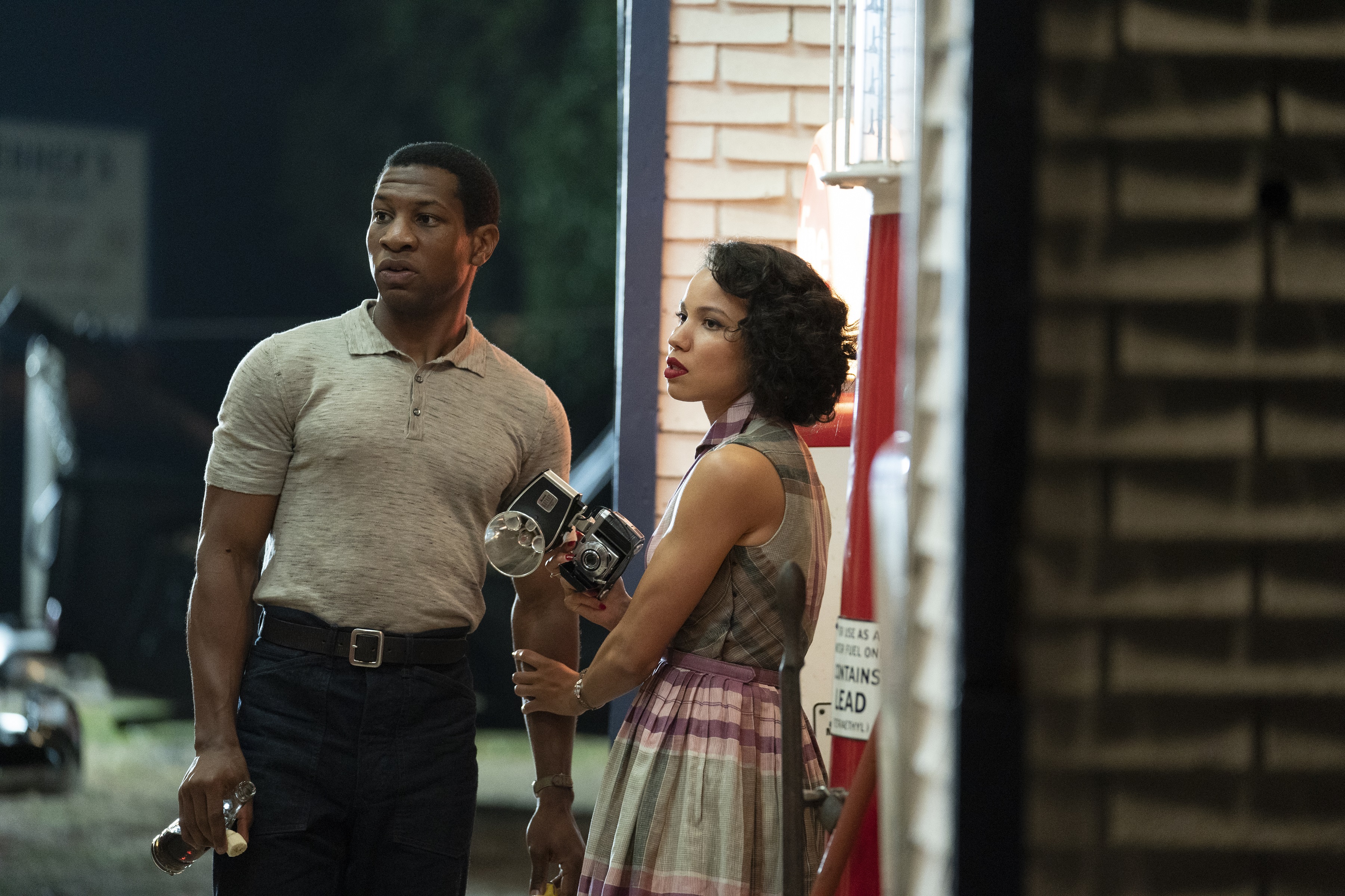 While holding a camera in one hand, Jurnee Smollett grabs Jonathan Majors' arm with her other hand as they look off from Season 1 of LOVECRAFT COUNTRY released in 2020.