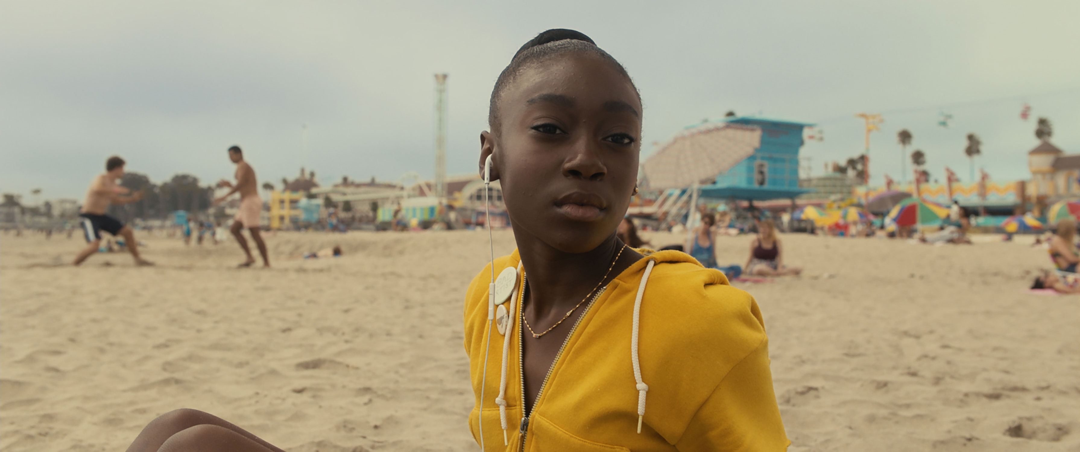 Shahadi Wright Joseph in the 2019 film US sitting on the beach wearing a sweatshirt and headphones.