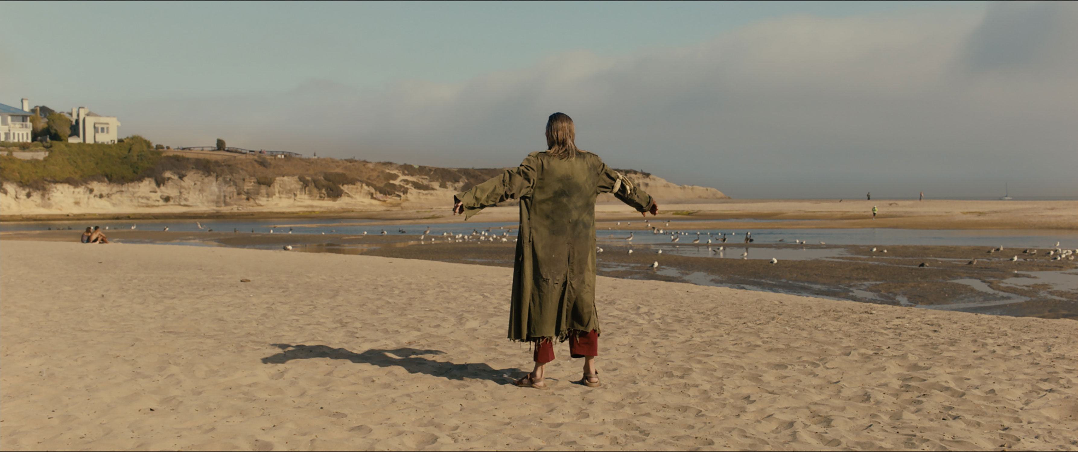 Alan Frazier in the 2019 film US standing, arms extended, on the beach.