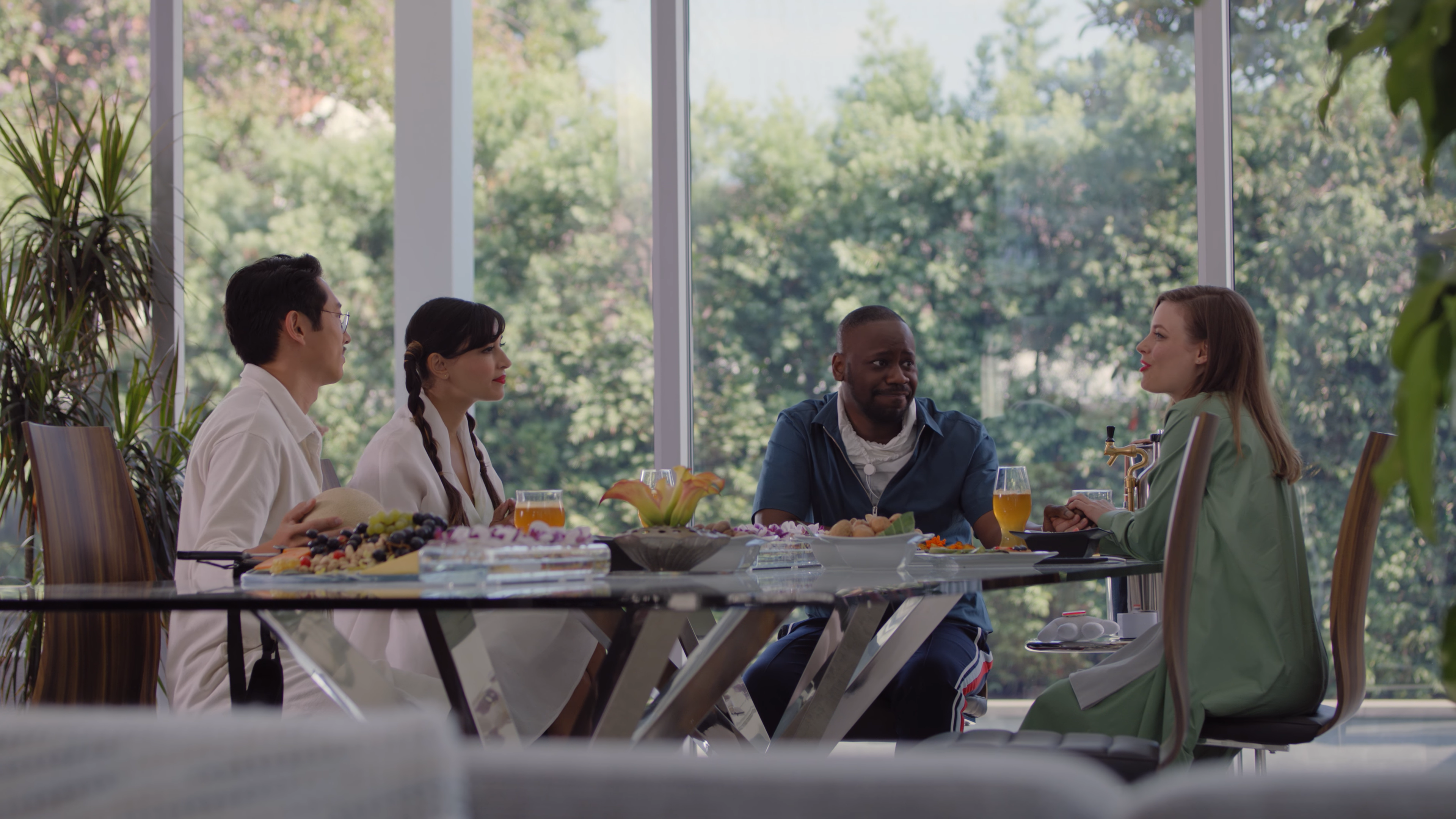 Gillian Jacobs, Hannah Simone, Malcolm Barrett, and Steven Yeun in the 2019 television series WEIRD CITY sitting at a glass dinner table, eating a lavish meal.