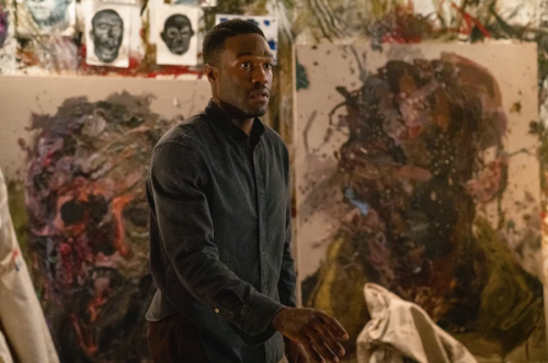 Man standing in front of two paintings in the movie Candyman.