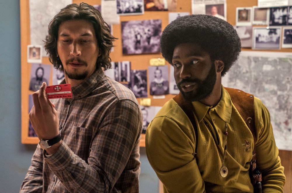 Adam Driver and John David Washington in the 2018 film BLACKKKLANSMAN sitting and looking at a card.