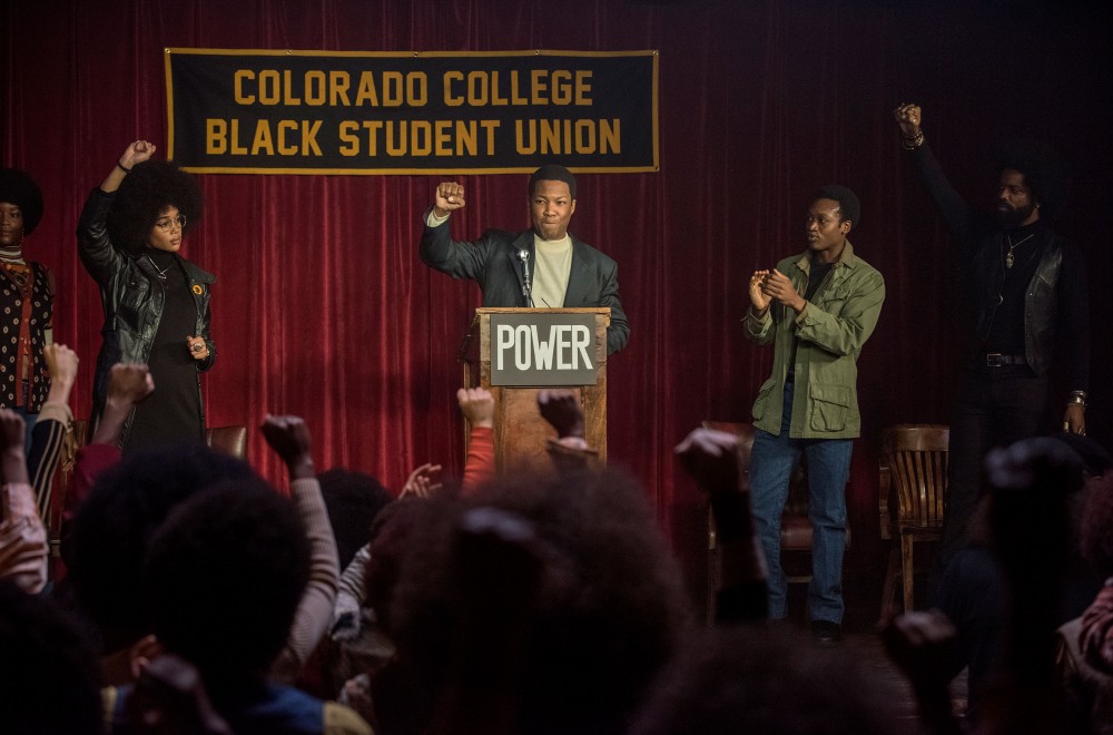 Corey Hawkins in the 2018 film BLACKKKLANSMAN stands at a podium with his fist raised.